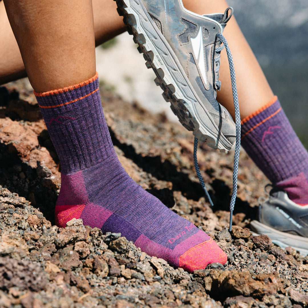 Close up shot of model sitting on the side of a mountain wearing the women's micro crew hiking sock in plum heather
