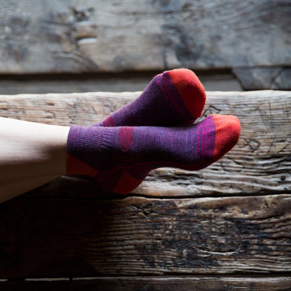 Close up image of a woman's feet, ankles crossed, wearing Women's Hiker Quarter Hiking Socks in Plum Heather, Lifestyle Image