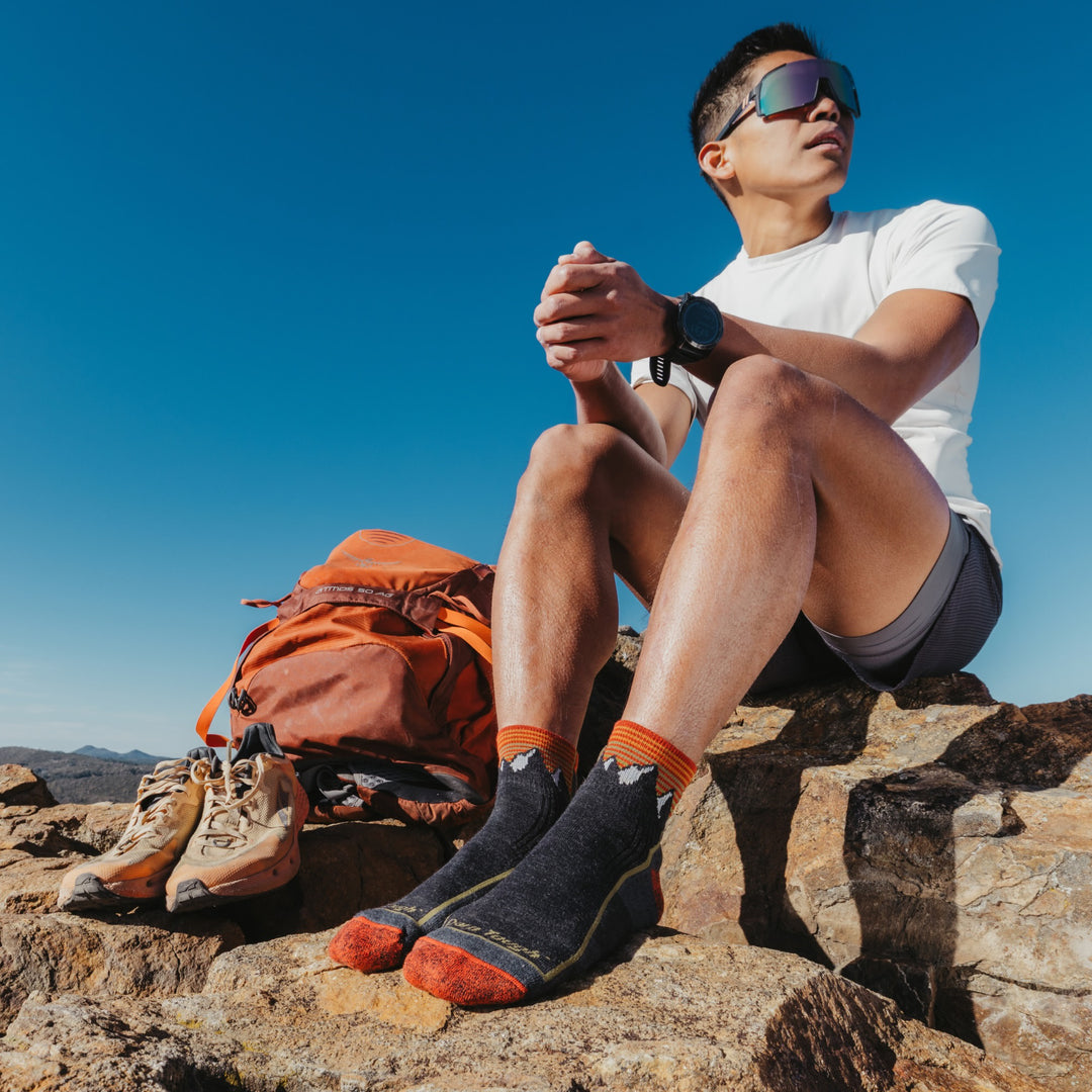 Model sitting on rock with gear next to them wearing the 1959 Quarter midweight hiker sock in mountain gray colorway
