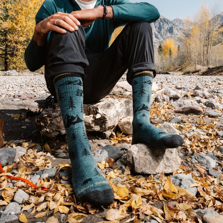 model sitting next to a rivered on a rock wearing the 1964 ABC boot sock in Teal 