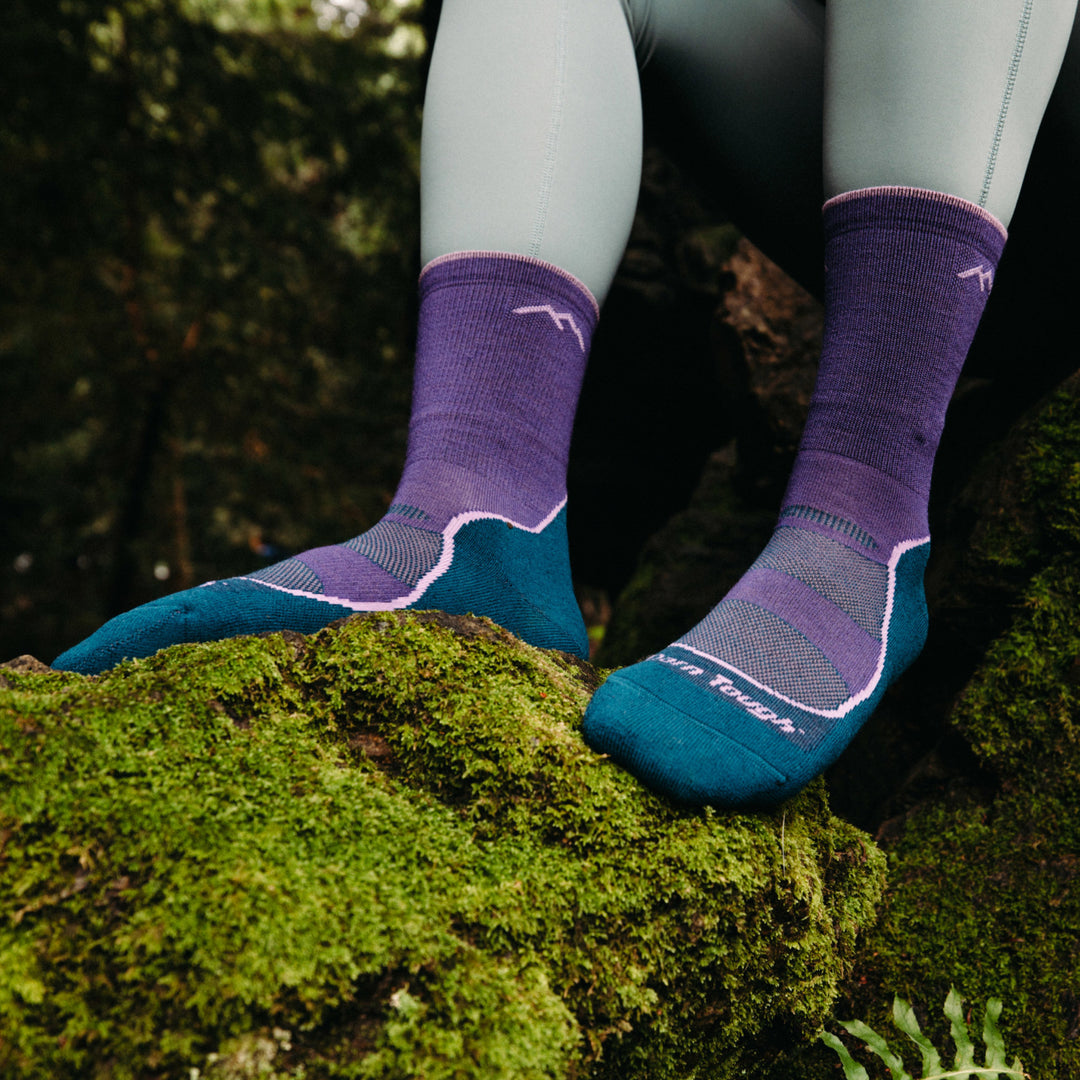 Models feet resting on a moss stone wearing the 1967 Light Hiker Micro Crew Hiking sock in Grape