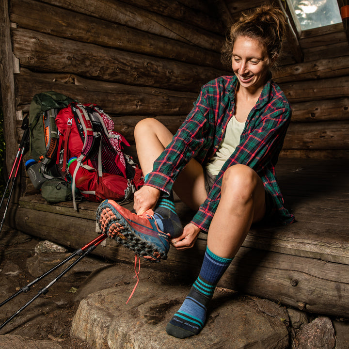 Backpacker up and ready to go, pulling on shoes over Her Spur hiking socks in blue