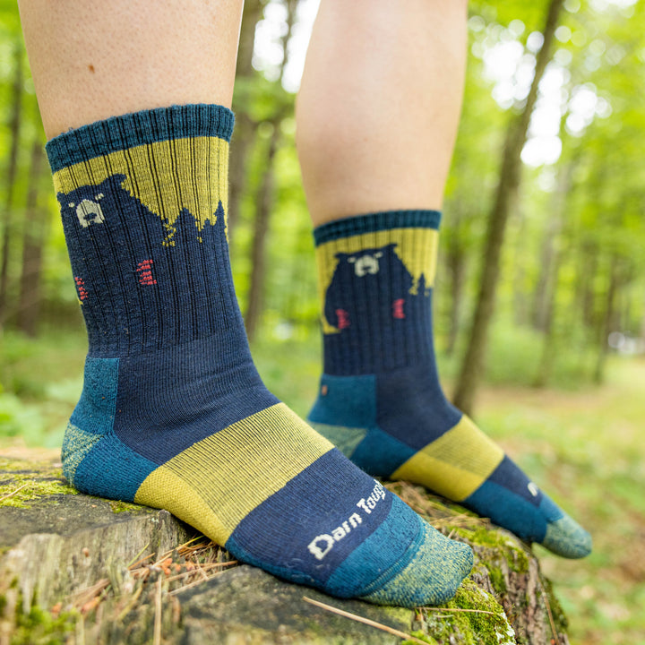 Model standing on a rock in the woods wearing the Beartown hiking sock in dark teal