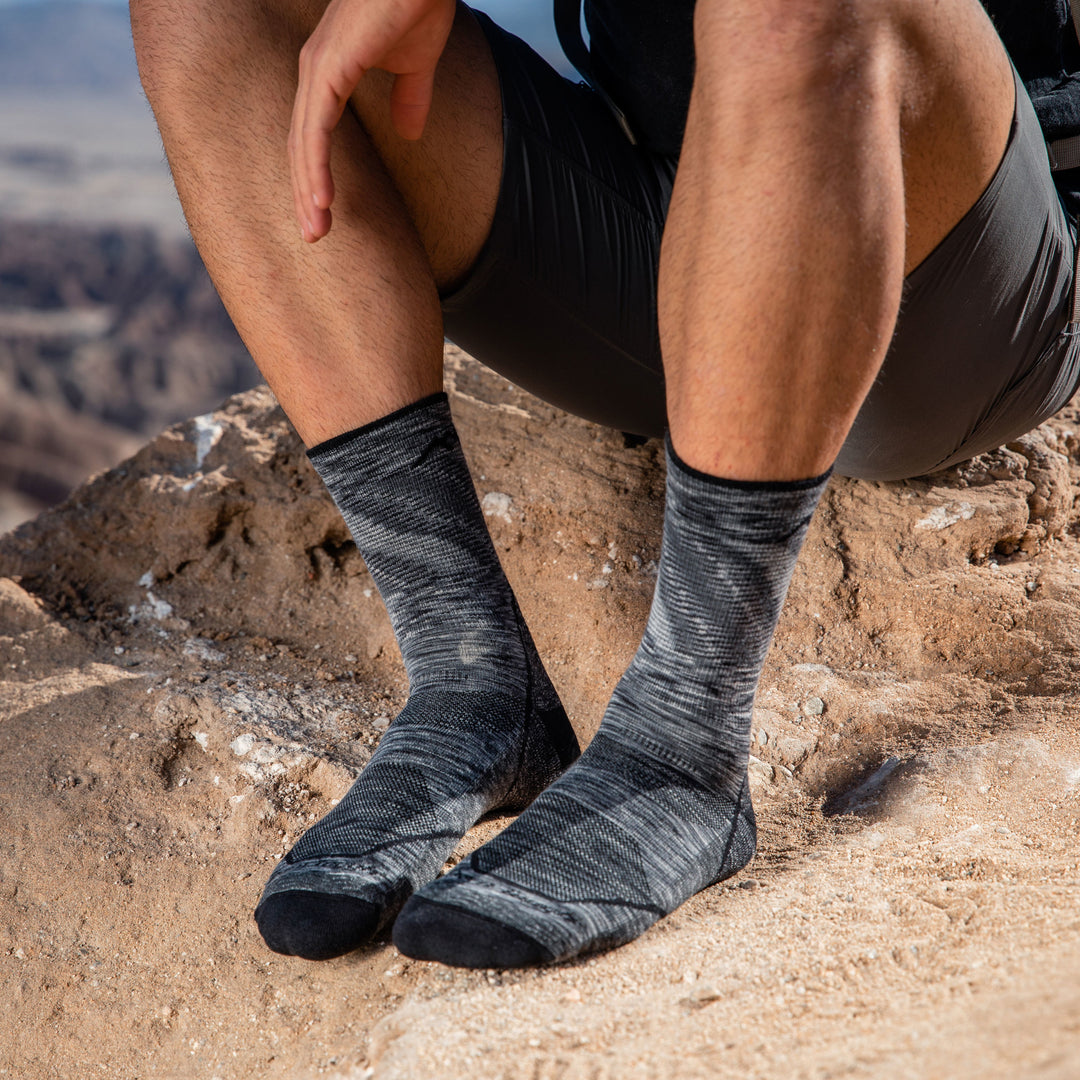 Close up shot of model sittting on a rock wearing men's light hiker micro crew hiking sock in space gray