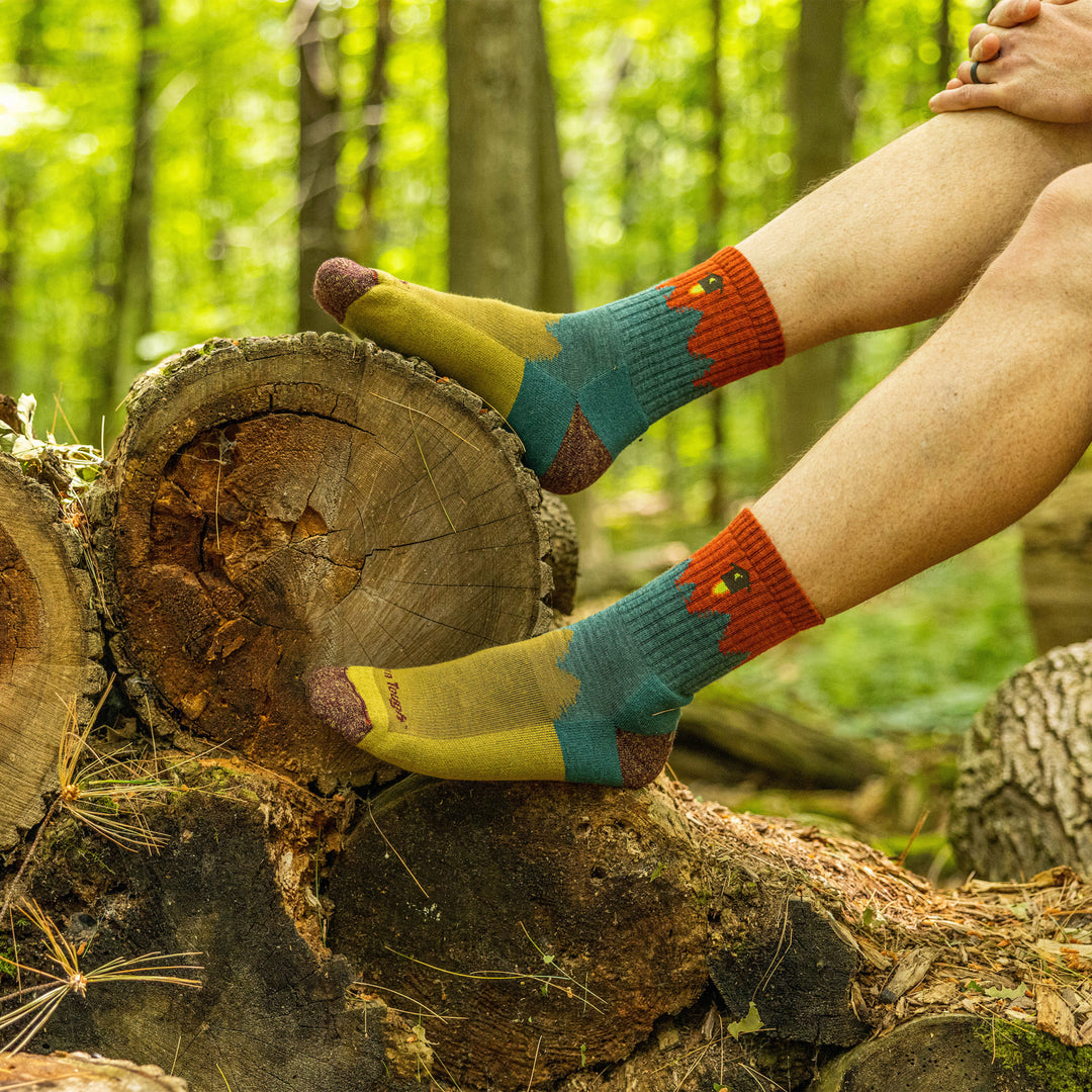 Close up shot of model sitting on a log in the woods wearing the men's number 2 micro crew hiking sock in teal