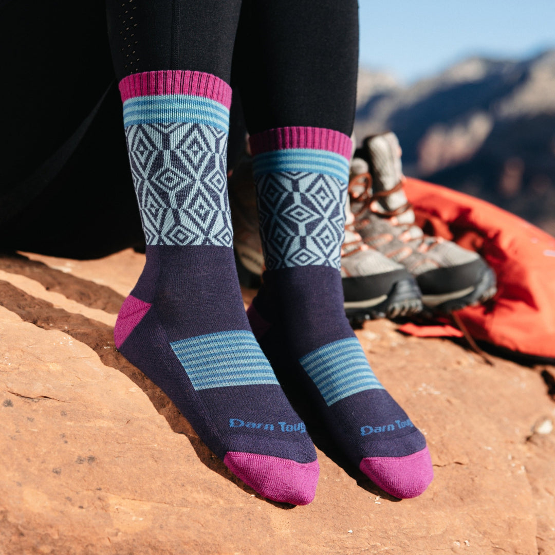 Model wearing 1977 socks in Blackberry colorway without shoes against tan desert rocks