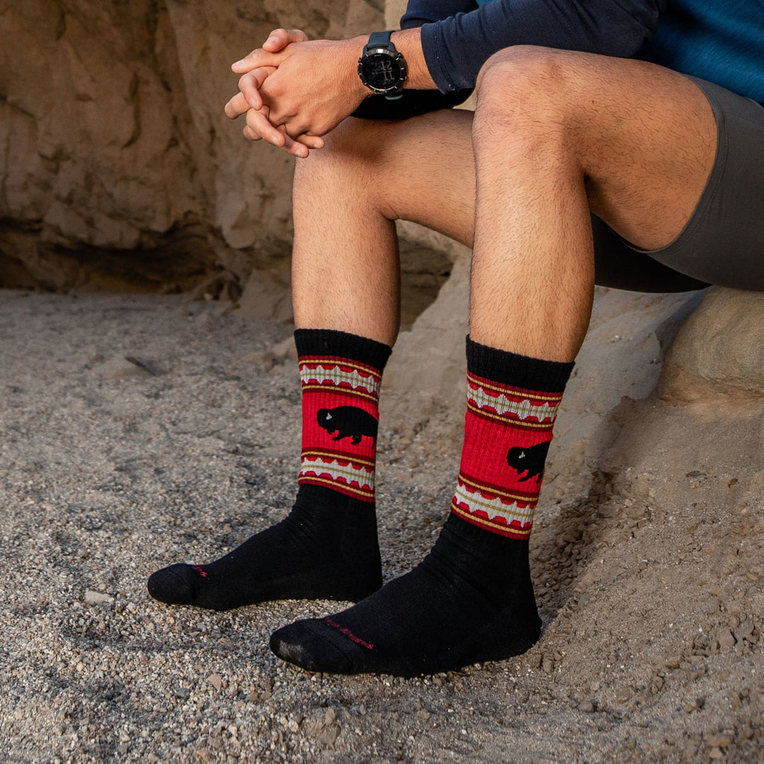 Side shot of model sitting on a rock outside wearing men's vangrizzle boot hiking sock in black