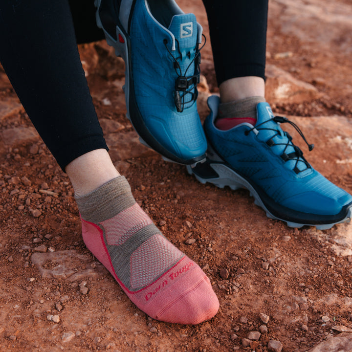 Close up of model wearing 1986 socks in Canyon colorway with blue running shoe on one foot against red desert dirt