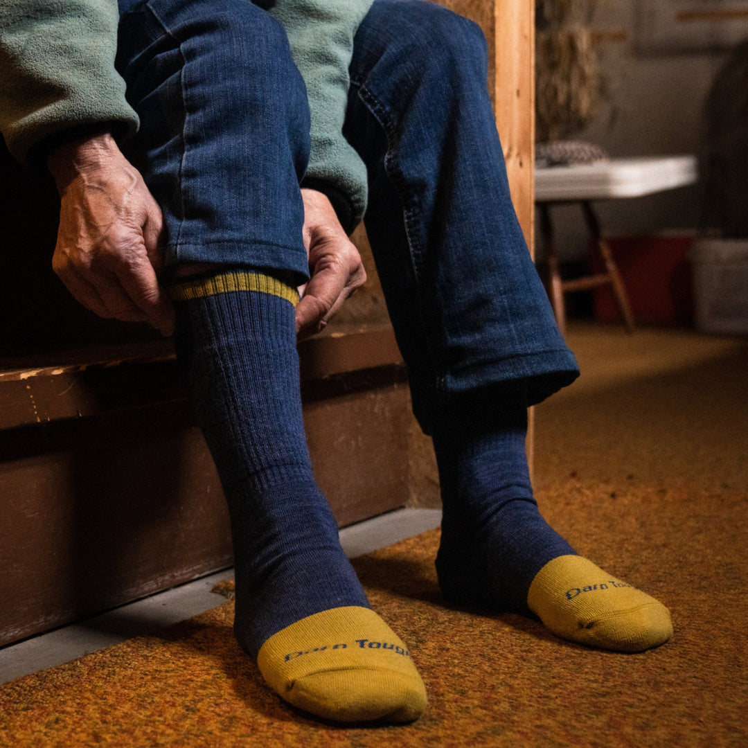 Close up shot of model sitting on indoor stairs pulling up 2015 socks in indigo colorway without shoes on