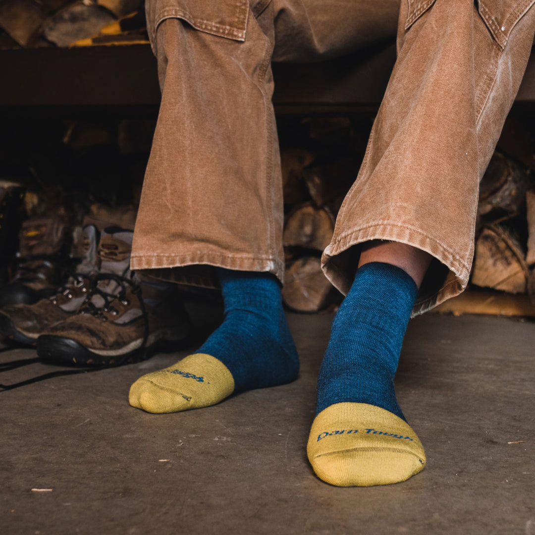 Close up shot of model sitting on bench in front of wood pile wearing 2016 socks in indigo colorway