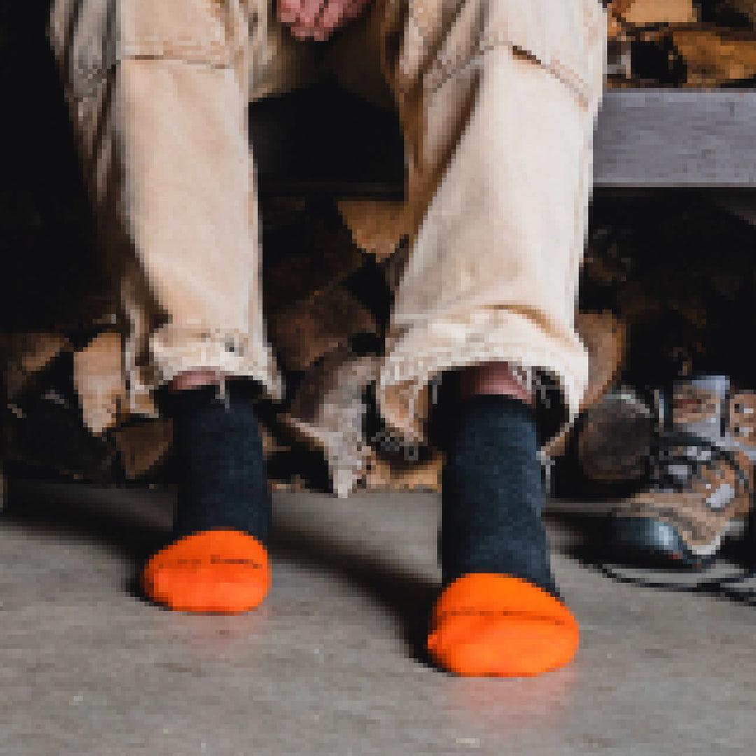 Close up shot of model sitting on bench in front of woodpile and wearing 2205 socks in graphite colorway without shoes on