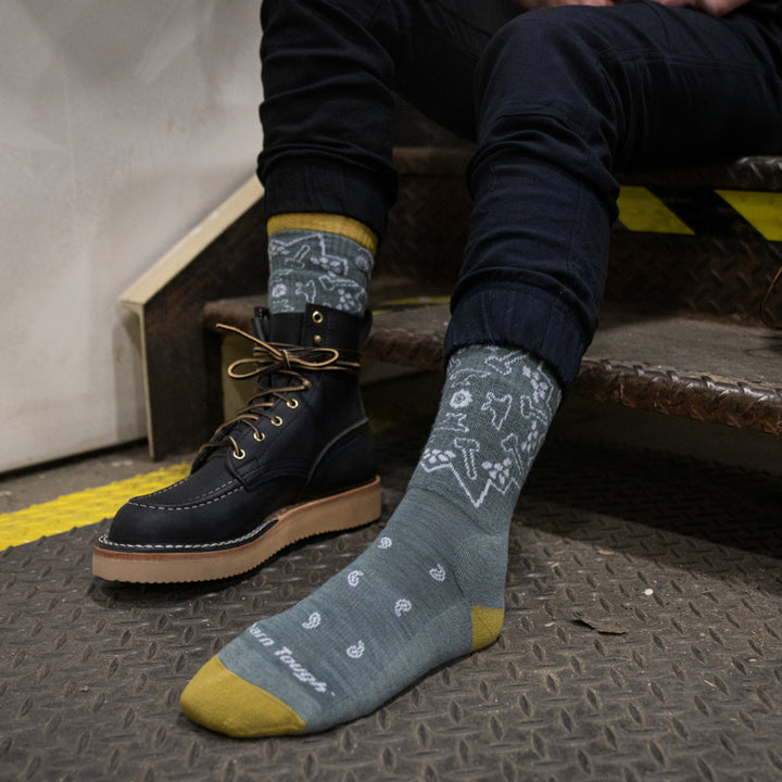 Models feet on metal steps with one shoe off wearing the 2206 Forged Midweight boot work sock in Seafoam