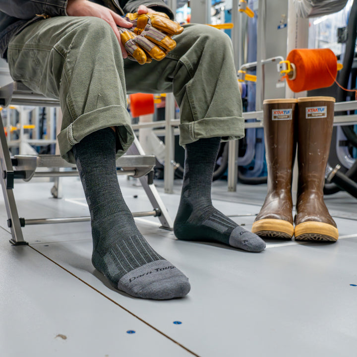 Model siting on step ladder next to rubber boots wearing the 2209 Stanly K boot sock in Gravel 