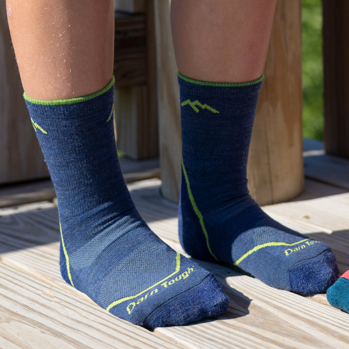 Close up shot of model sitting on a deck outside wearing the juniors light hiker micro crew hiking sock in denim blue