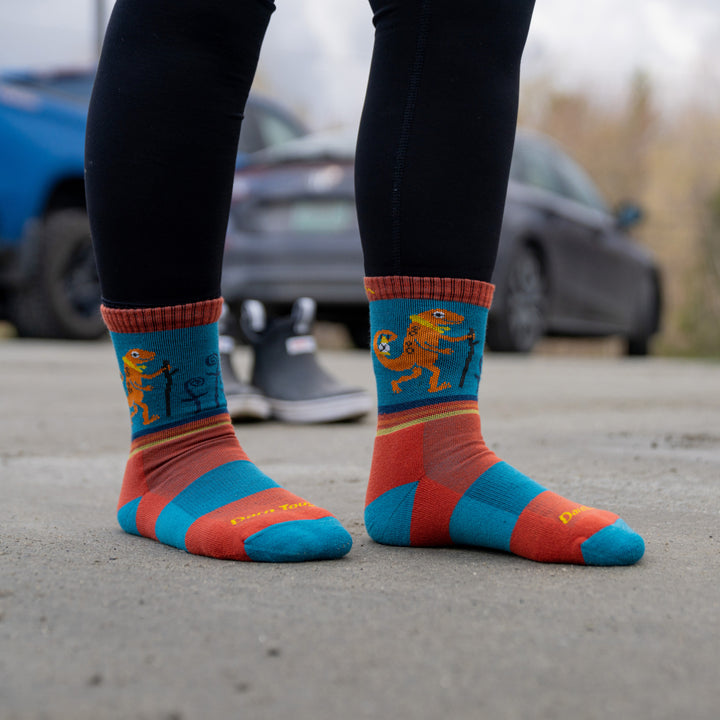 Close up shot of model standing on concrete without shoes wearing 3043 socks in Lava colorway with hiking salamander illustration facing outwards
