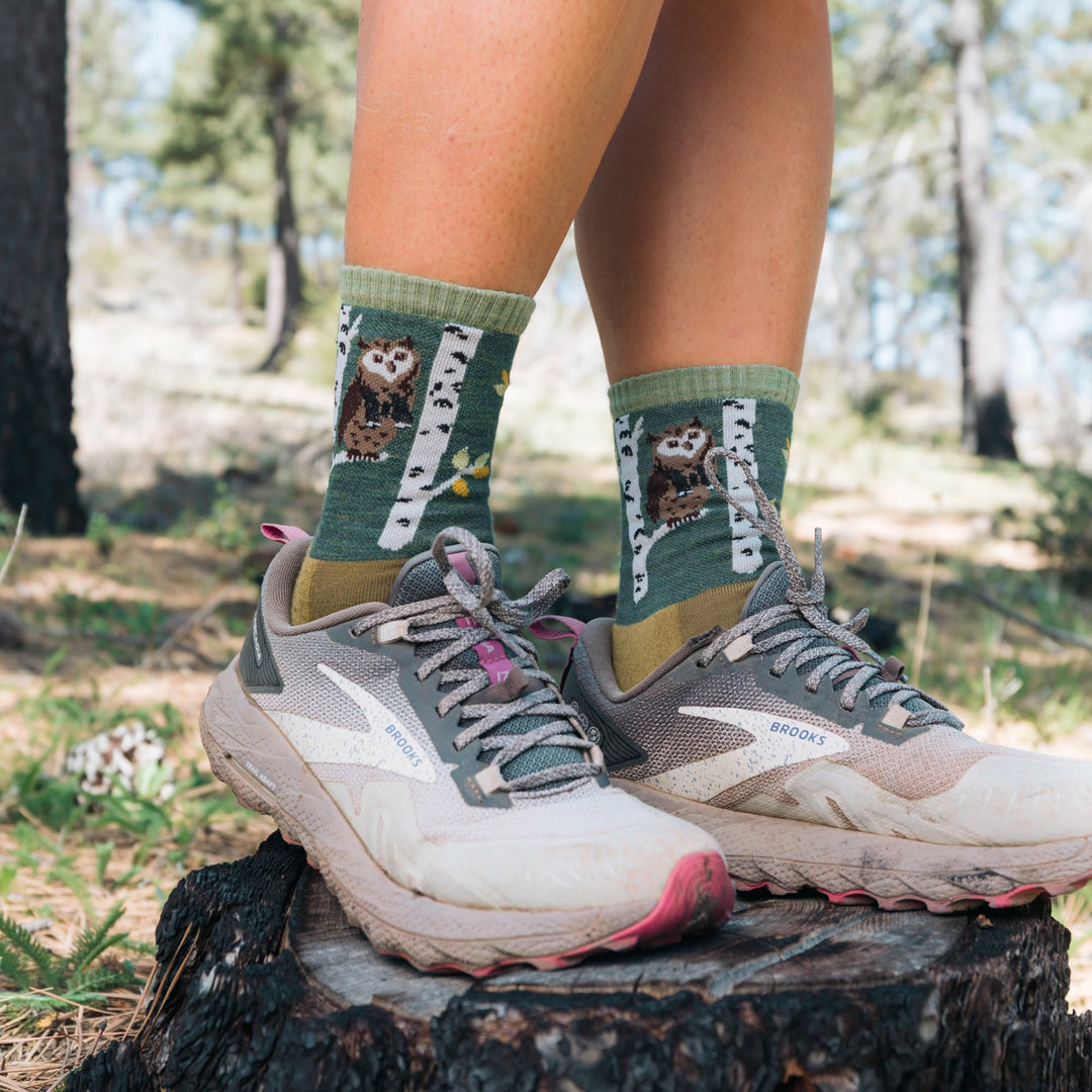 model standing on stump in sneakers wearing the 5001 critter club micro crew hiking sock in owl green 