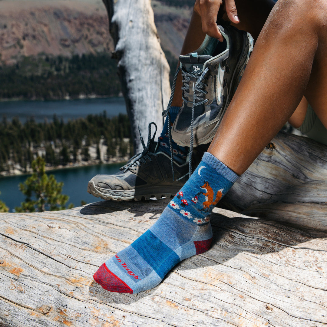 Shot of model sitting on top of a mountain wearing the women's critter club micro crew hiking sock in vapor blue