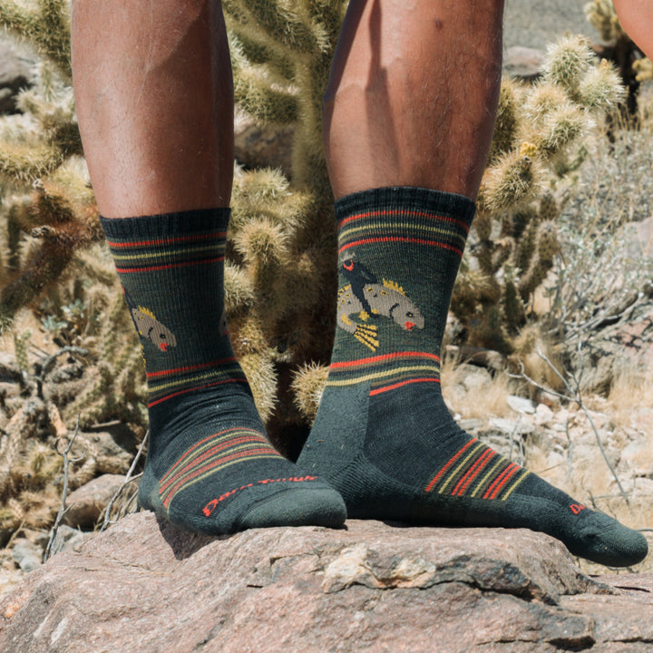 models feet standing on a rock in desert wearing the limited edition willoughby in rodeo green featuring a cowboy riding a fish