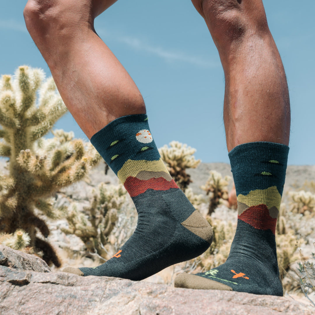 close up of models feet in the desert with one foot raised wearing the 5051 spaced out lightweight micro crew hiking sock in charcoal colorway