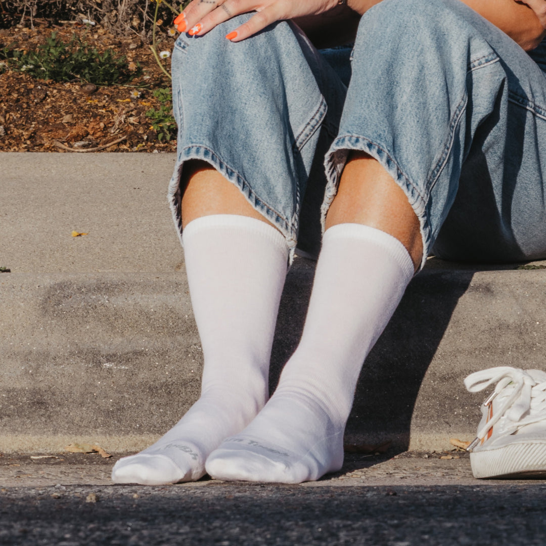 close up model sitting on sidewalk, feet on ground, wearing the 6012 solid lightweight lifestyle crew sock in white colorway