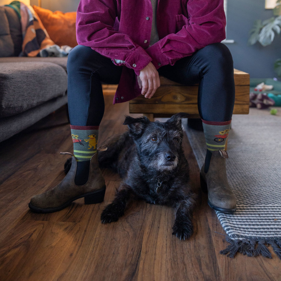 Model sitting in living room with a black dog wearing the women's animal haus crew lfiestytle sock in herb