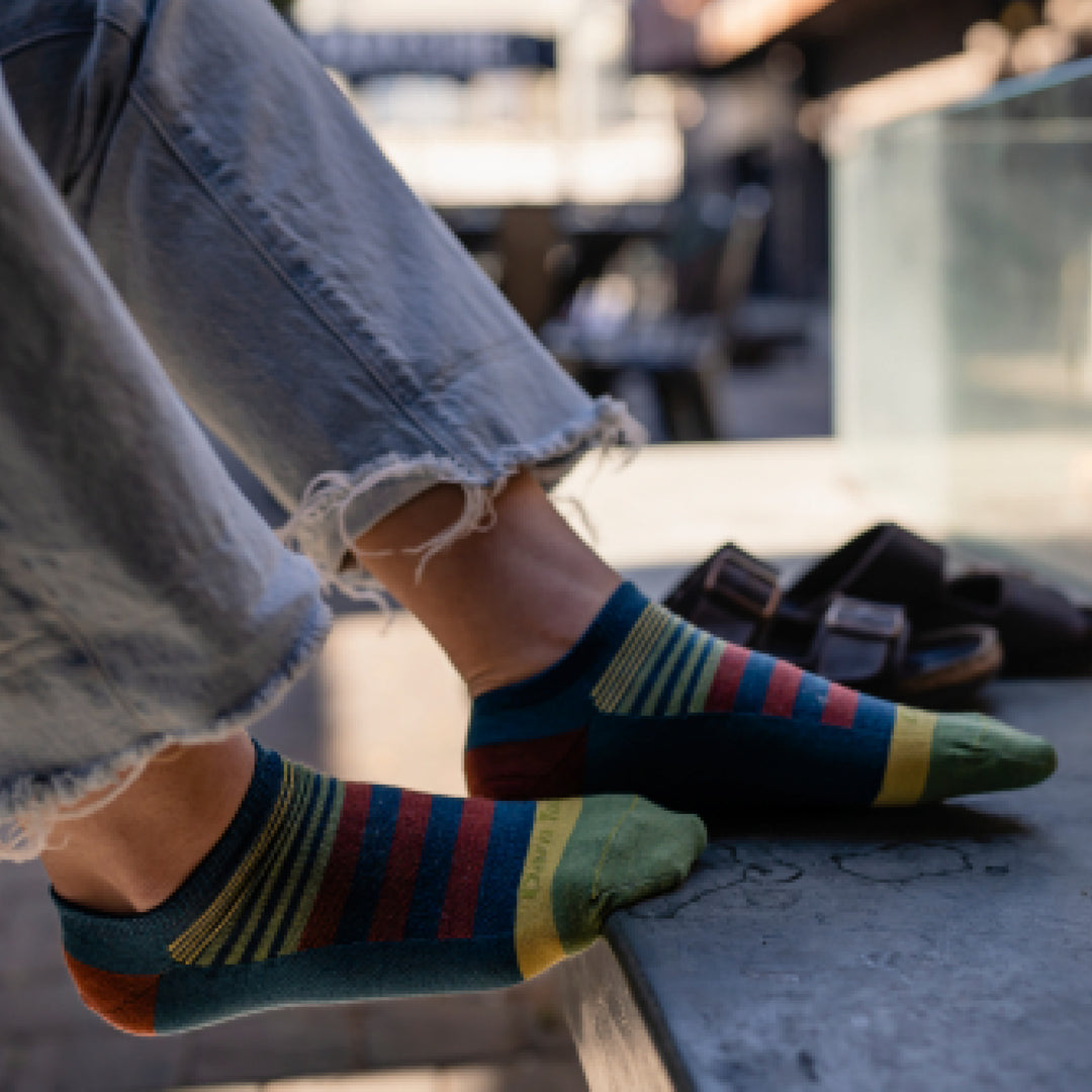 Model wearing 6073 socks in Dark Teal colorway without shoes with feet propped up on ledge