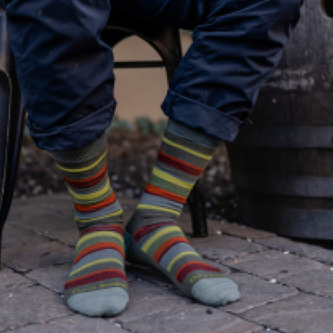 Close up shot of model sitting on a stool with rolled up blue pants and wearing 6090 socks in cedar colorway without shoes on