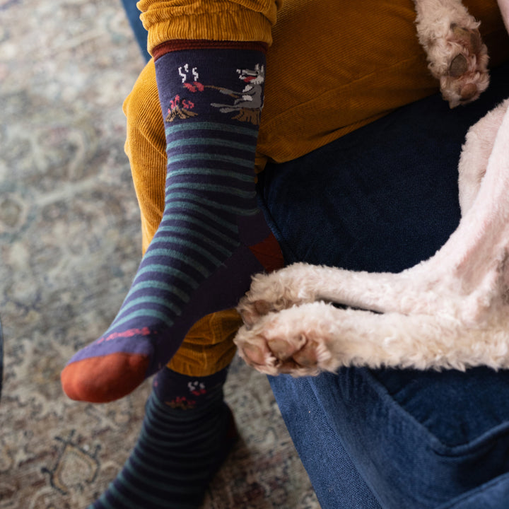 up close on model image of the 6096 Blackberry featuring an orange heel/toe purple green stripe body and wolf roasting hot dogs over fire at the cuff