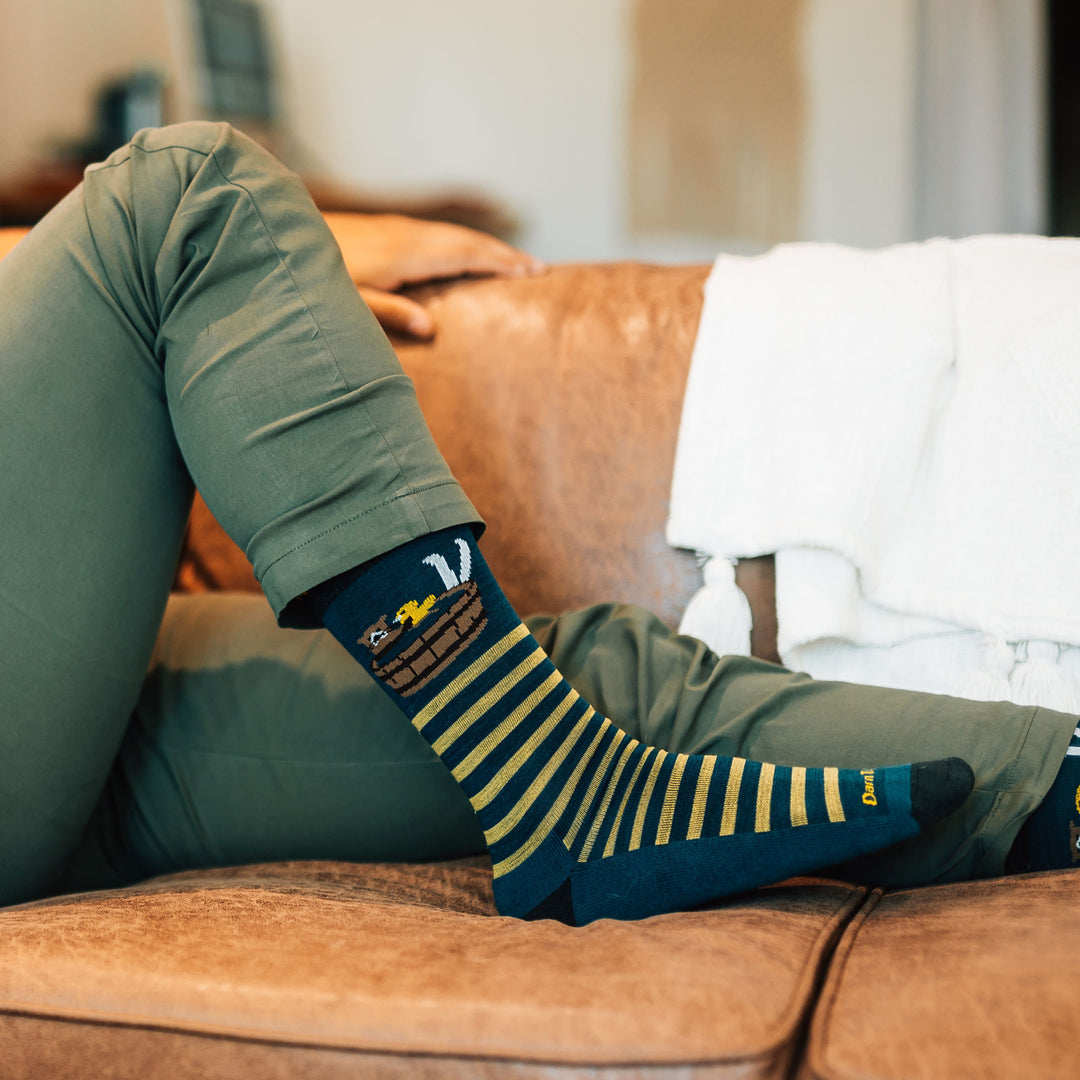 Close up on model with foot on couch wearing the 6096 Wild life lifestyle sock in dark teal