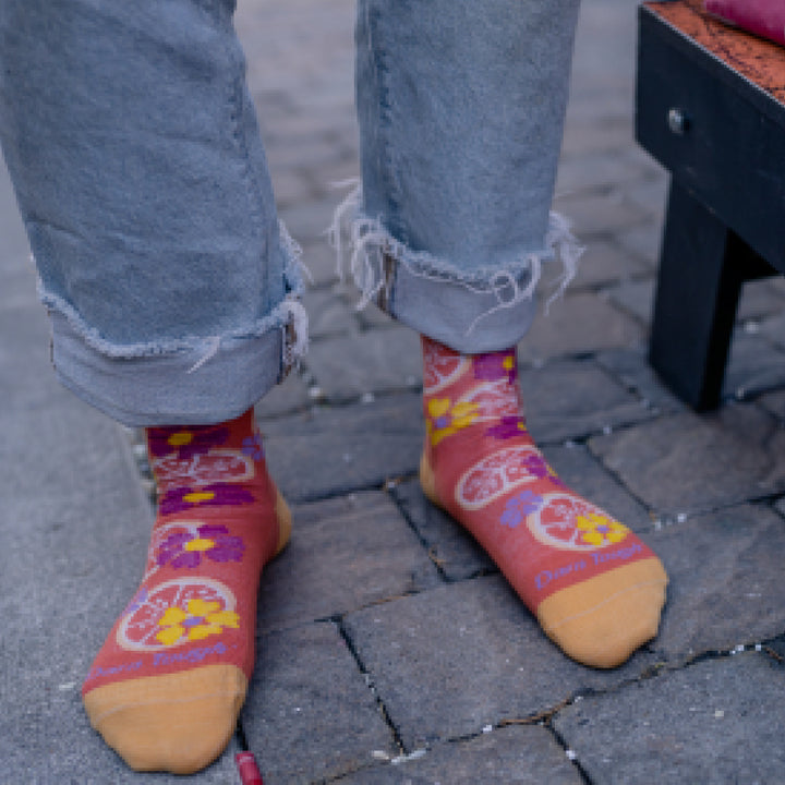 Close up shot of model wearing  rolled up jeans and 6102 socks in grapefruit colorway and standing on brick patio 