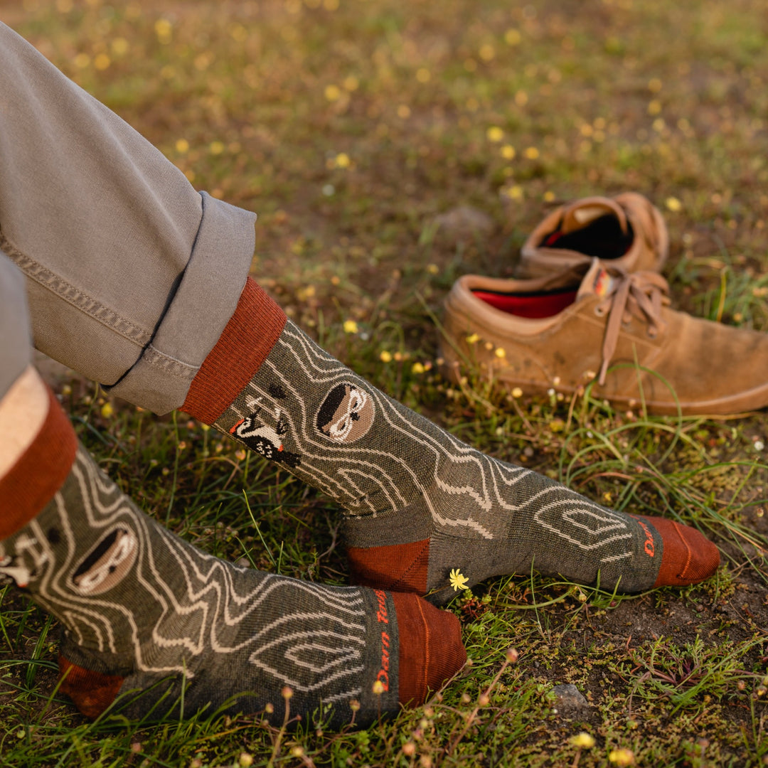 Close up shot of model wearing rolled up gray jeans and 6111 socks in forest colorway sitting in a meadow