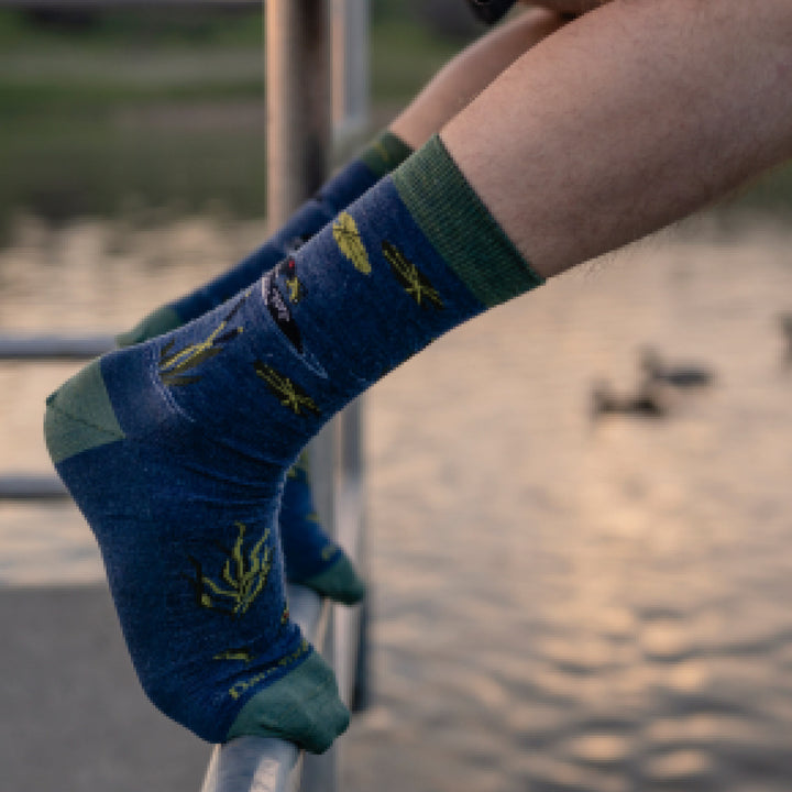 Close up shot of model sitting on a railing wearing 6112 socks in Denim at dusk with water in the background