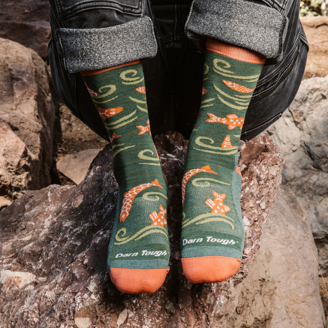 Model sitting on rock wearing the 6122 Homer Crew Lifestyle Sock in Kelp