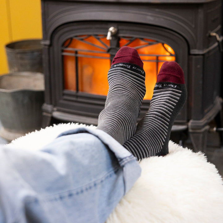 close up image of mens feet on ottoman in front of wood stove wearing 6134 microstripe crew lightweight charcoal sock