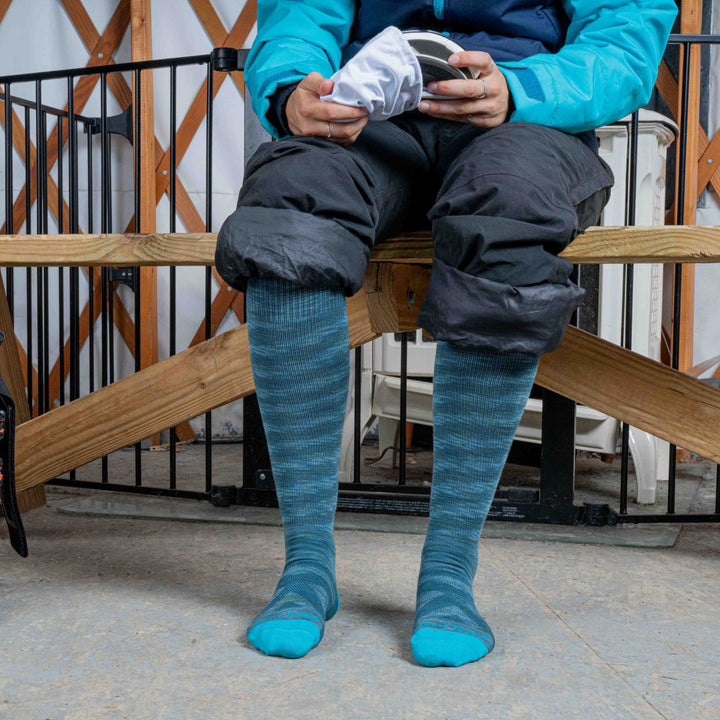 Woman on a bench with pants rolled up wearing the Women's RFL Ultra-Lightweight Ski and Snowboard Socks in Neptune