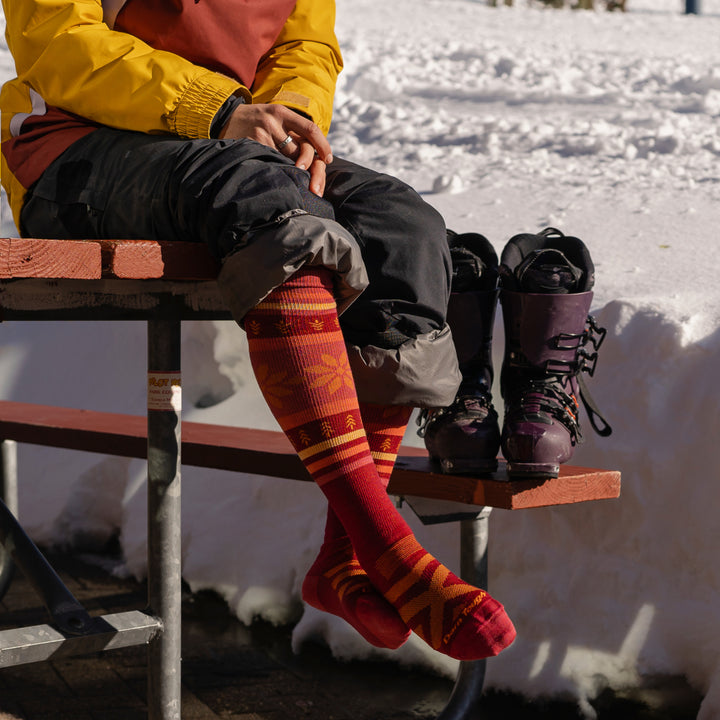Woman sitting with ski boots wearing Women's Alpine Over-the-Calf Lightweight Ski and Snowboard Sock in Burgundy