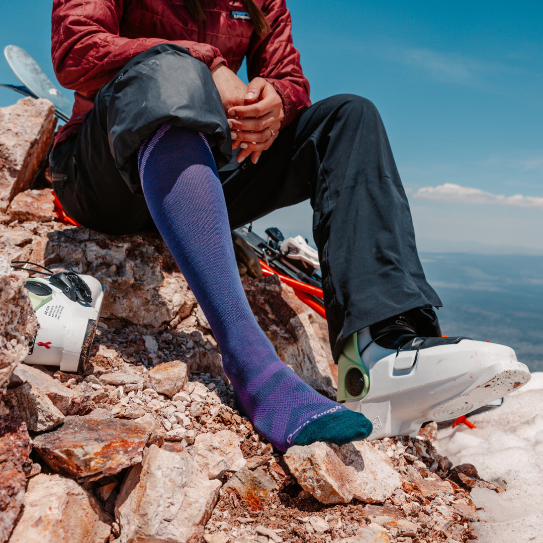 Close up on model wearing 8035 Iris resting on rock with back foot in ski boot 