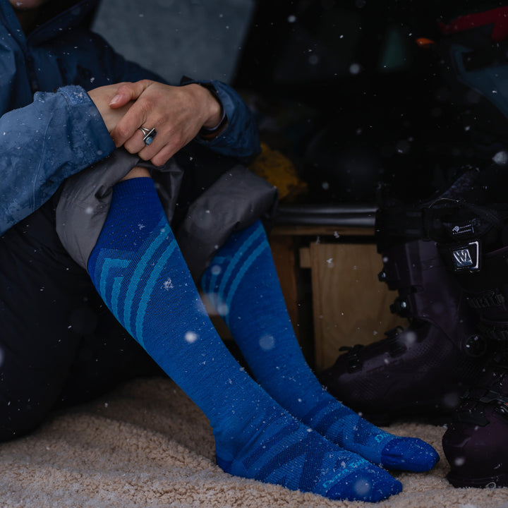 Woman sitting inside while it snows in her Women's Peaks Over-the-Calf Ultra Lightweight Ski and Snowboard Socks