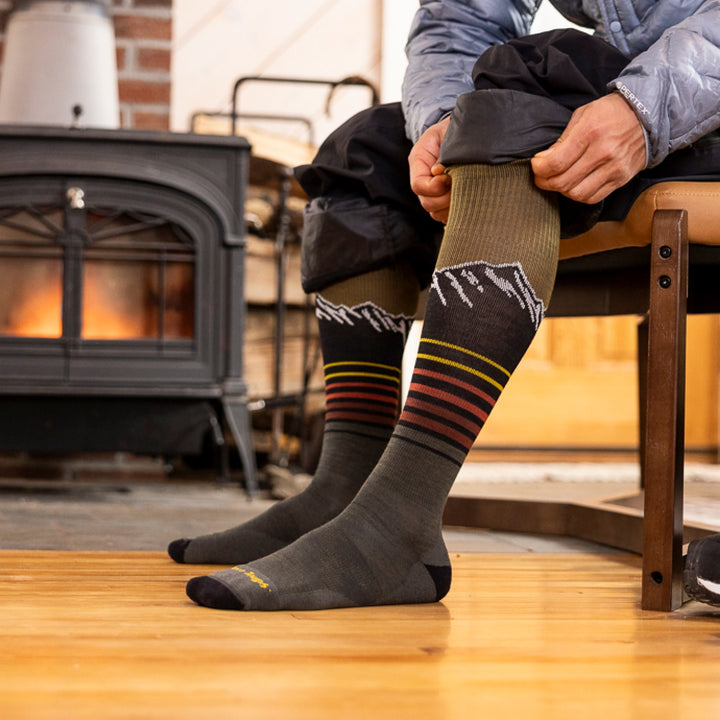 close up of model sitting on bench with snowpant legs rolled up showing 8052 steep lines OTC lightweight with cushion sock forest