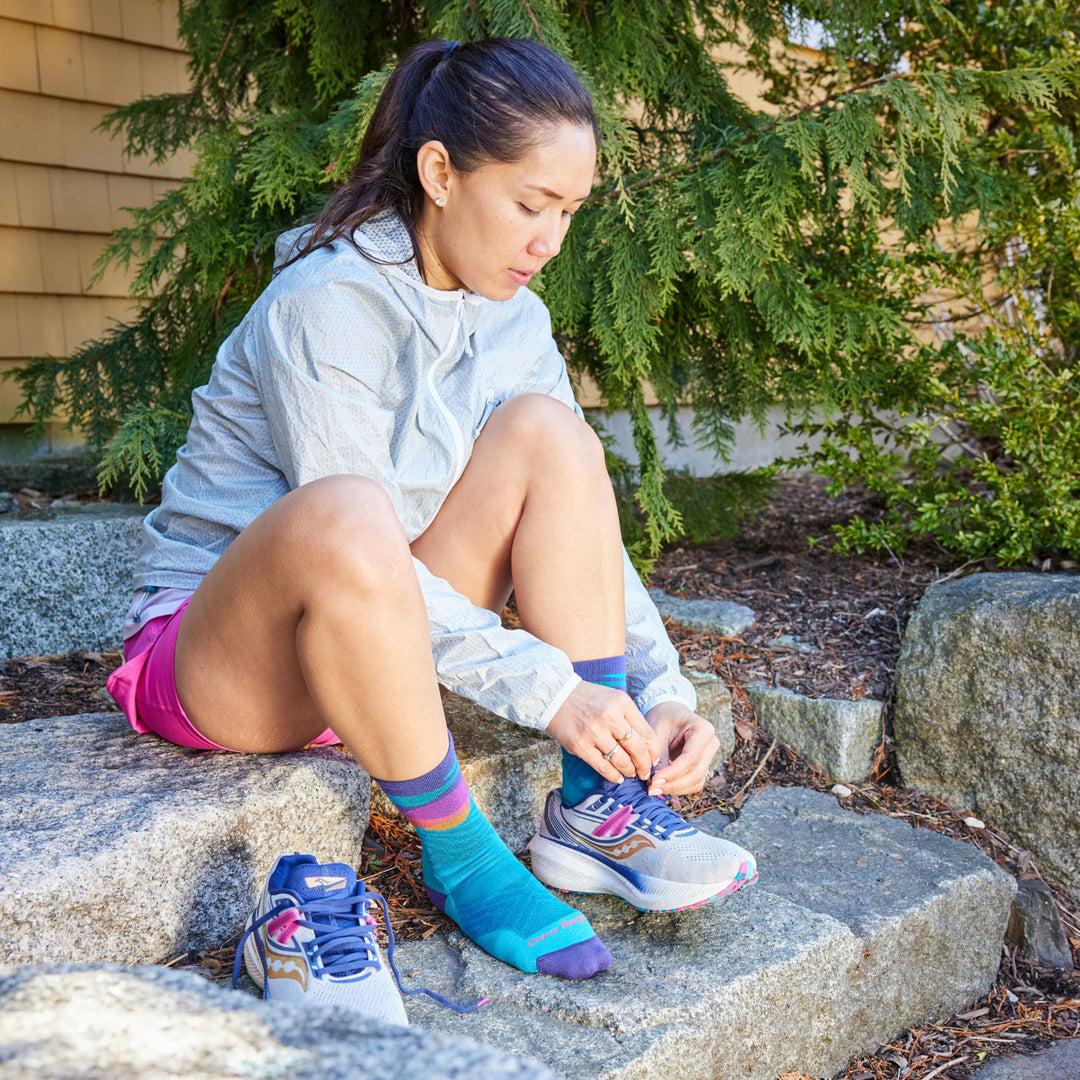 Model sitting on granite steps putting sneakers on wearing the 1067 Mirnavated Micro Crew running socks in cascade