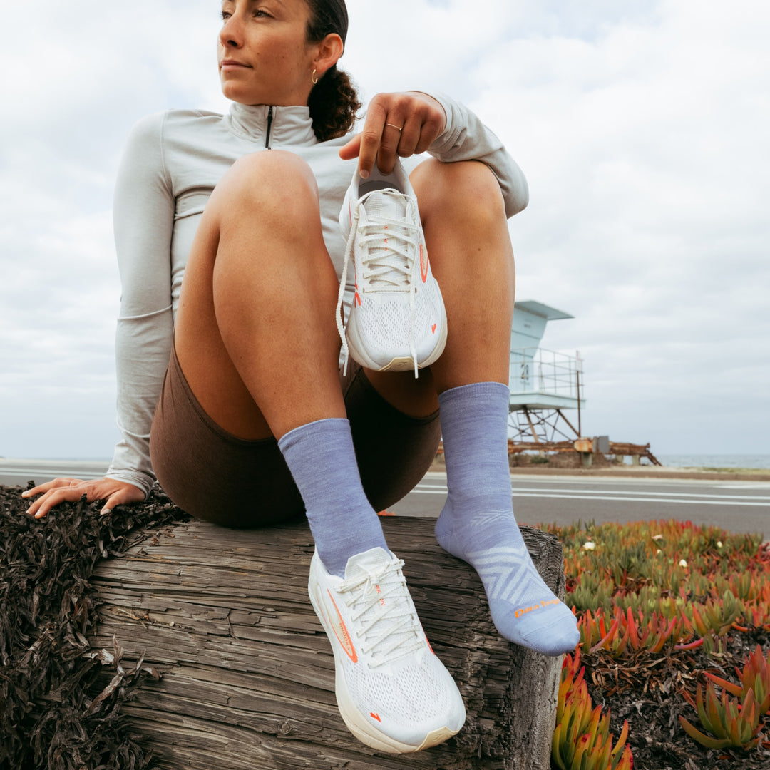model sitting on log holding one shoe wearing the 1068 micro crew running sock in vapor colorway