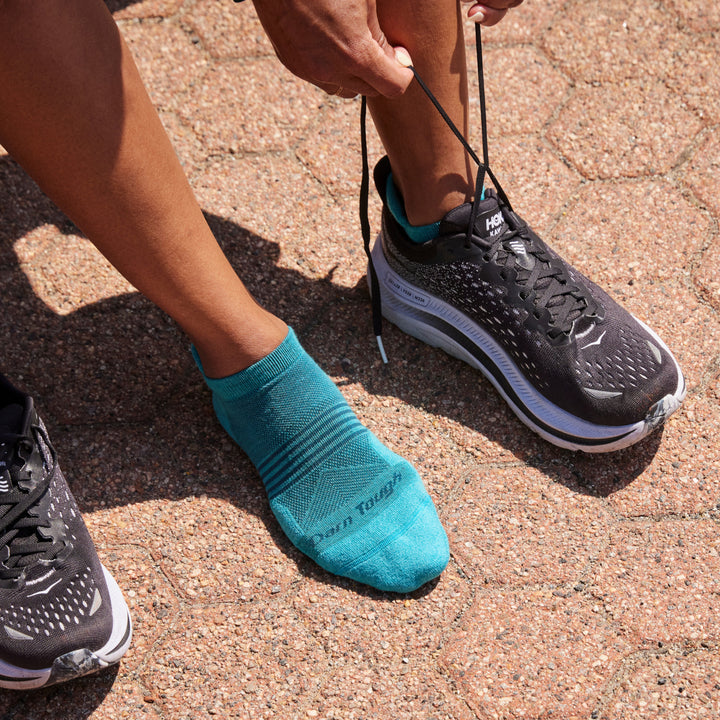 Close up shot of model wearing 1112 socks in cyan colorway and lacing up black running shoe on left foot