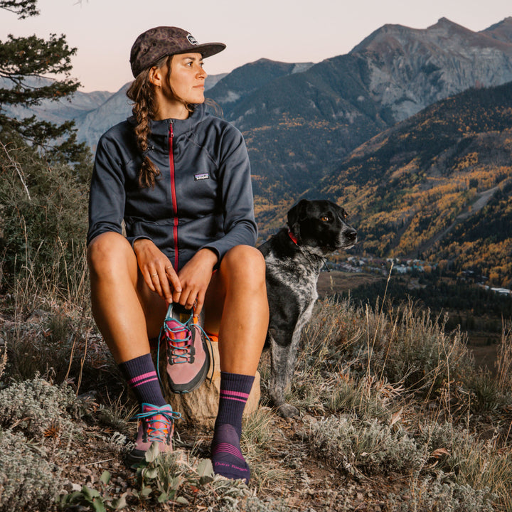 Model sitting on rock atop a mountain holding one shoe wearing 1114 Element micro crew running sock in Blackberry