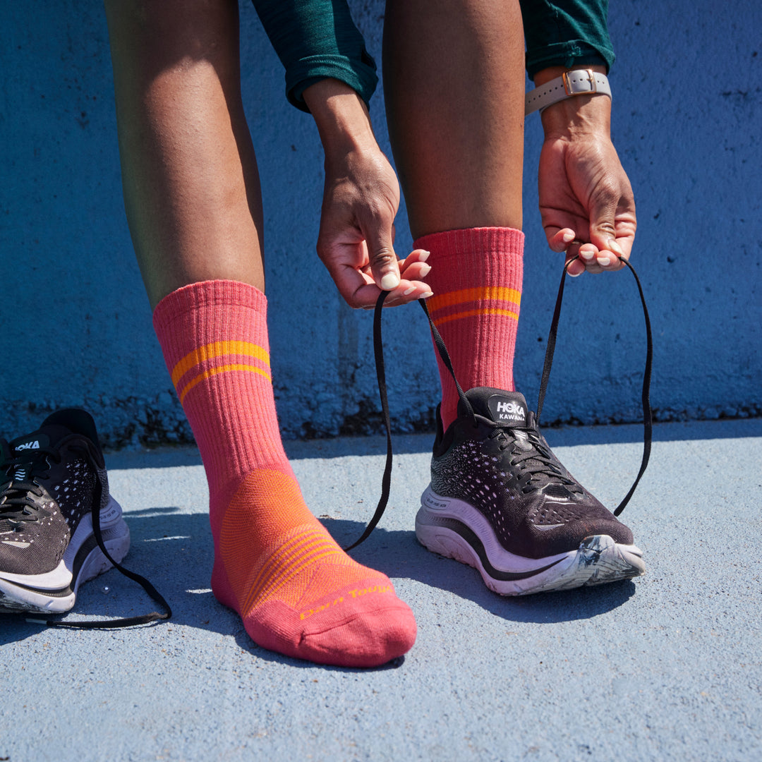 Close up shot of model wearing 1114 socks in Raspberry colorway lacing up black running shoes against blue painted concrete background