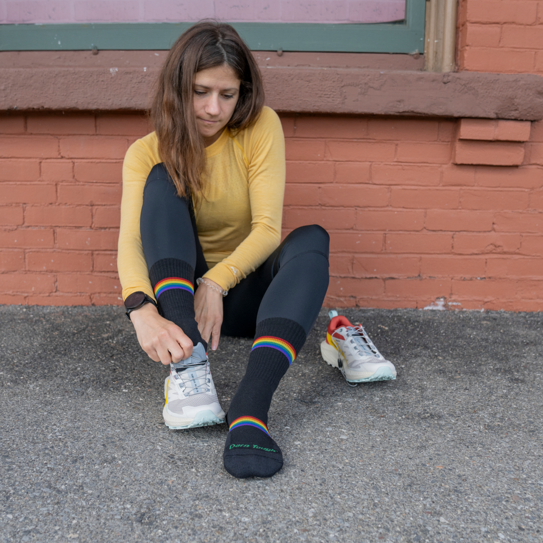 Shot of model Wearing 1115 Prism Micro Crew Running socks sitting against brick wall and pulling on white running shoes.
