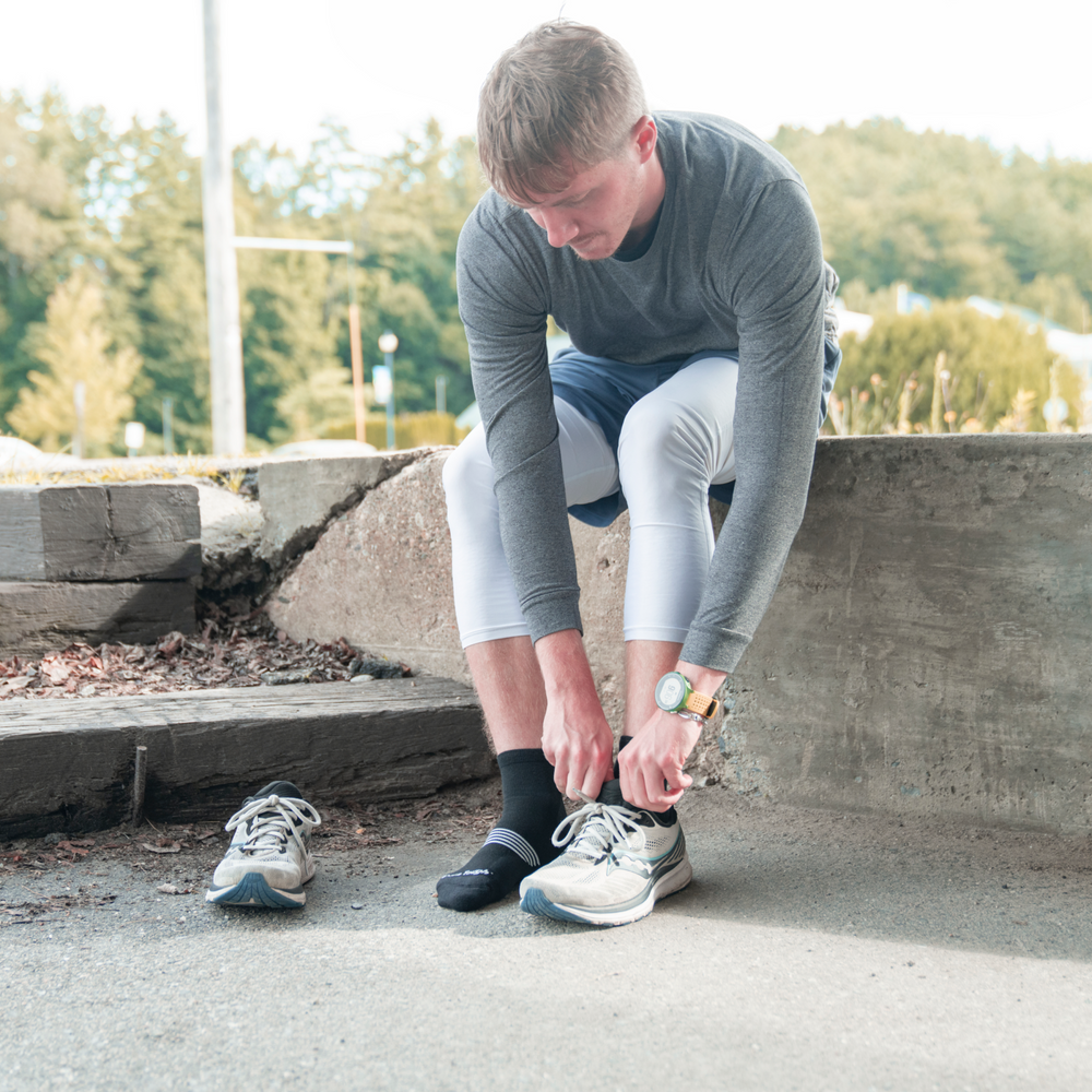 A runner getting ready by putting on his left shoe over his Darn Tough Element Quarter Run Socks in black