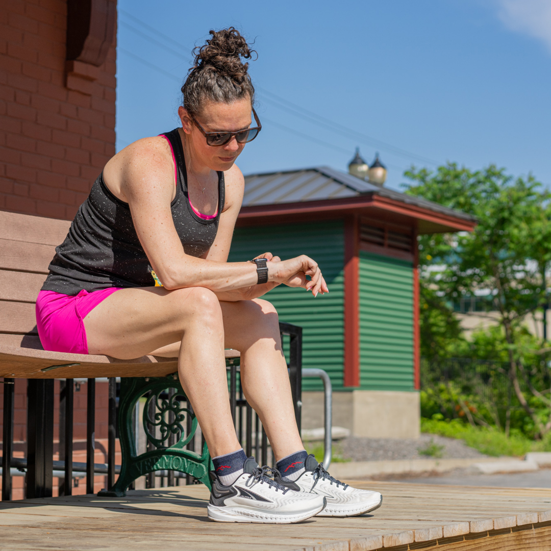 Model sitting on bench checking her watch wearing the 1201 natural running sock in her sneakers