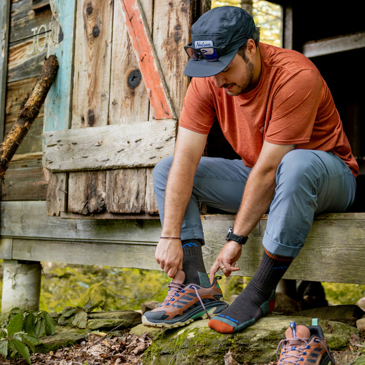 Model sitting in door way putting on shoes wearing the 1466 micro crew hiker in Hickory 