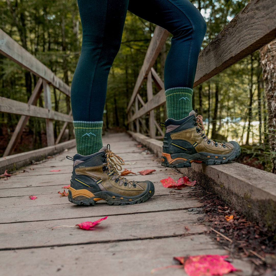 On model image standing on wooden bridge in hiking shoes wearing the 1903 micro crew hiking sock in evergreen