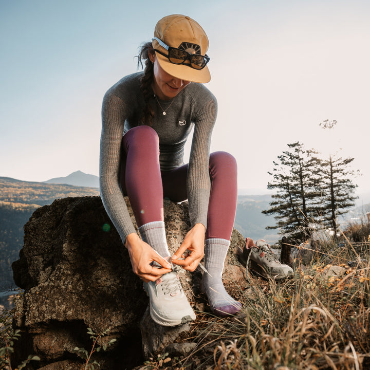 model sitting on a rock putting her shoes on wearing the 1903 micro crew hiker in light denim 